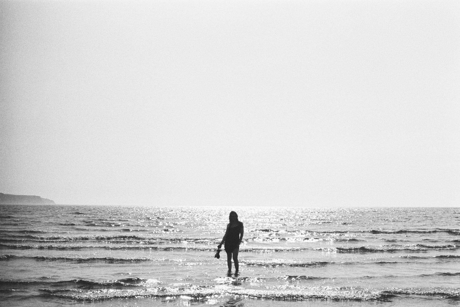 Person standing in shallow water at the beach with a minimalistic design.